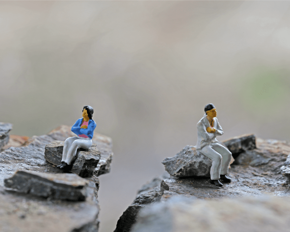 Two clay figures with arms folding sitting apart from each other with backs turned