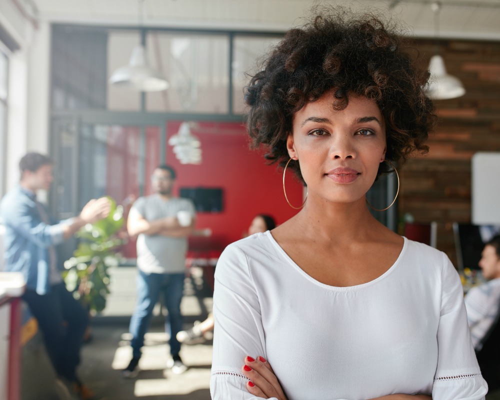 Portrait of woman standing in busy creative office looking at camera. Attractive female creative professional in design studio.