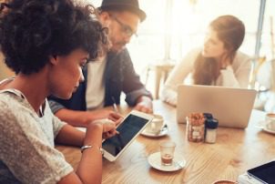 Close up portrait of young african woman using digital tablet with her friends sitting by at a cafe table. Group of young people sitting at a coffee shop with digital tablet and laptop.