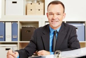 Steuerberater sitzt im Büro am Schreibtisch mit Akten und Taschenrechner