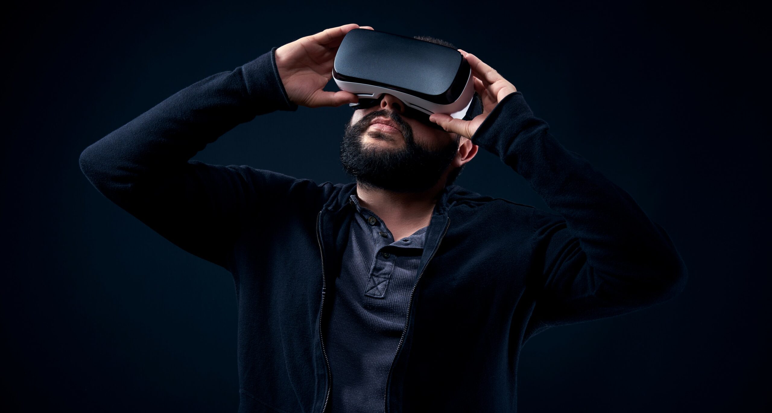 Young hipster bearded man wearing virtual reality goggles. Black background studio VR concept.