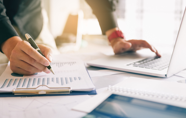Businessman holding pen and pointing paper chart summary analyzing annual business report with using laptop at room office desk.